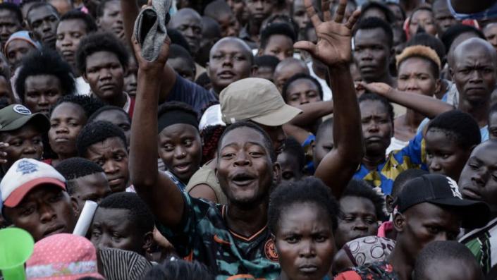 A packed crowd of people gathered together. There is one man in the middle smiling with his hands in the air - he looks jubilant.