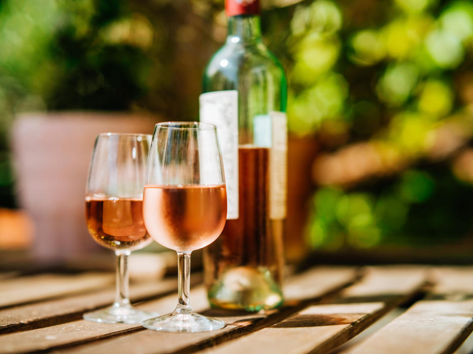 Glass of rose on a table in sunlight, blurred greenery in the background