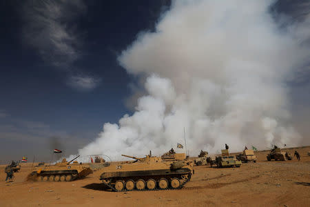 Iraqi army gather after the liberation of a village from Islamic State militants, south of Mosul, during an operation to attack Islamic State militants in Mosul, Iraq, October 21, 2016, as toxic smoke is seen over the area after Islamic State militants set fire to a sulphur factory. REUTERS/Thaier Al-Sudan