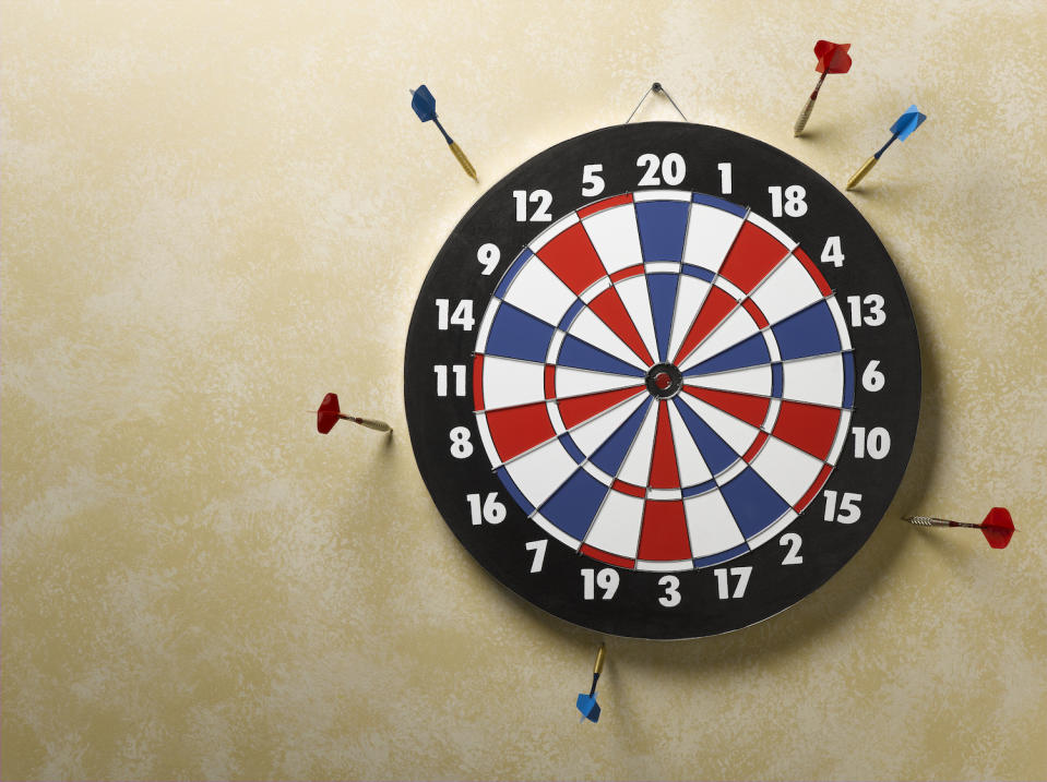 Red and blue darts in wall around red, white and blue dart board