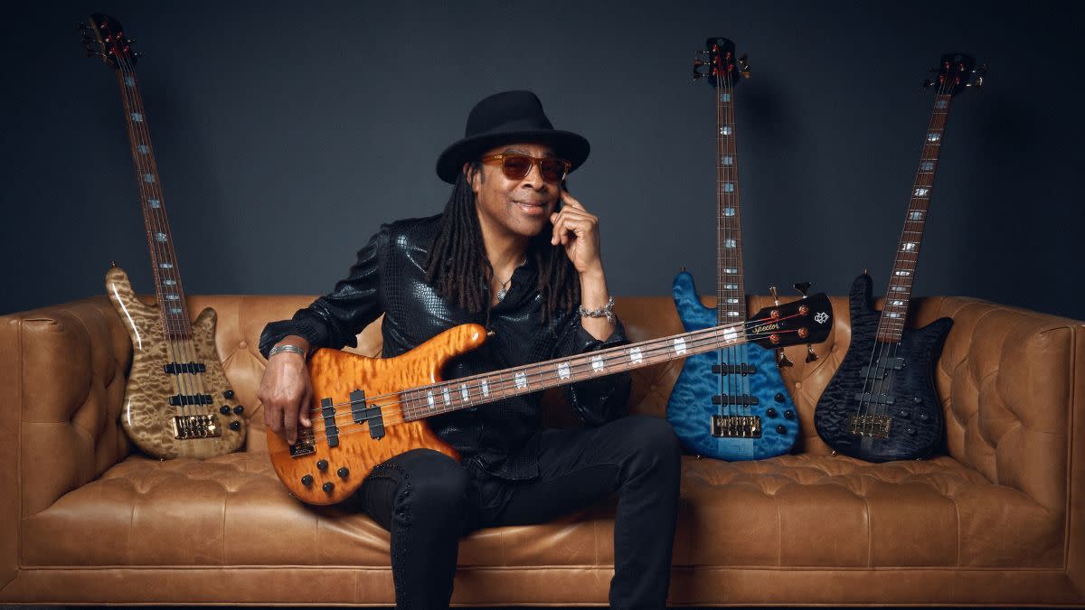  Doug Wimbish sitting on a sofa, holding one of his signature basses, with more of his signature Spector basses placed next to him. 
