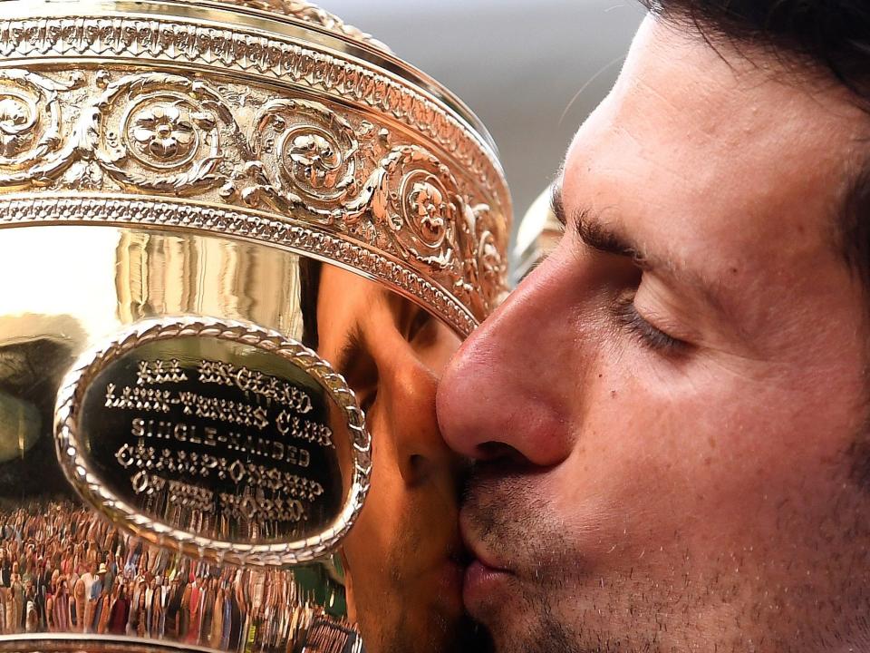 FILE - In this July 14, 2019, file photo, Serbia's Novak Djokovic kisses the trophy during the presentation after he defeated Switzerland's Roger Federer in the men's singles final match of the Wimbledon Tennis Championships in London. The All England Club says it plans to make a decision next week whether to postpone or cancel Wimbledon because of the coronavirus pandemic.  (Laurence Griffiths/Pool Photo via AP, File)