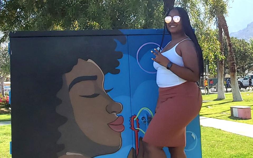 Palm Springs native La'Ronjanae Curtis stands by a mural of a person blowing bubbles.