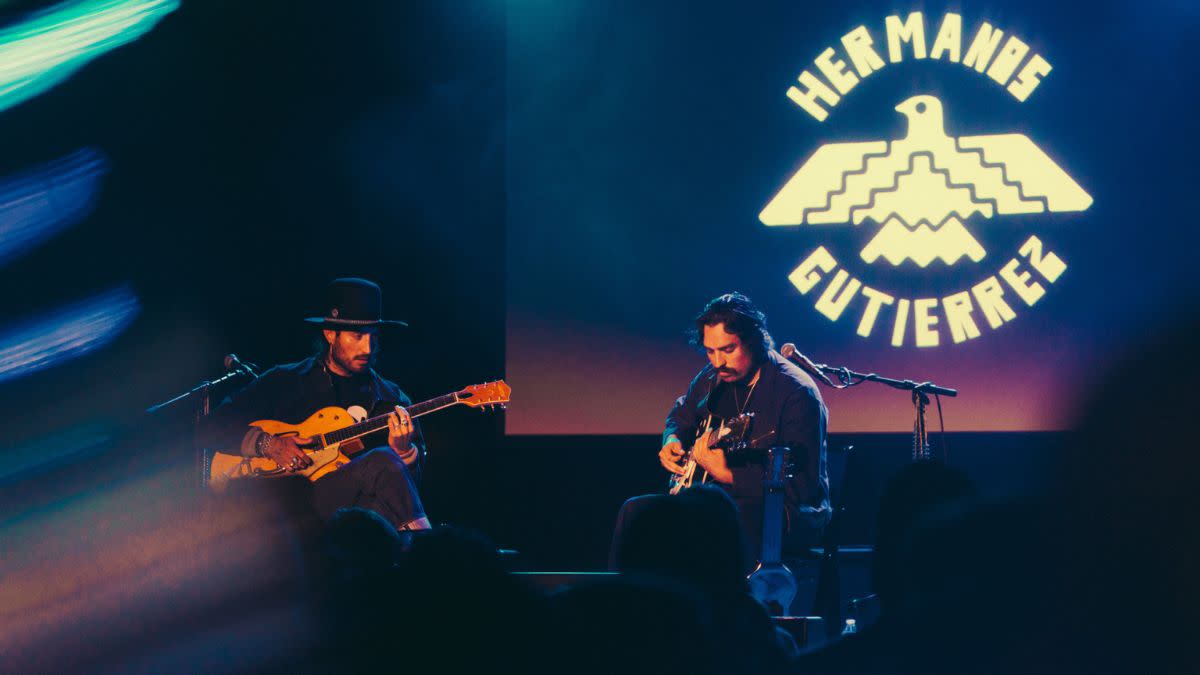  Guitar duo Hermanos Gutiérrez playing their guitars on stage with a projection of their logo at the back . 