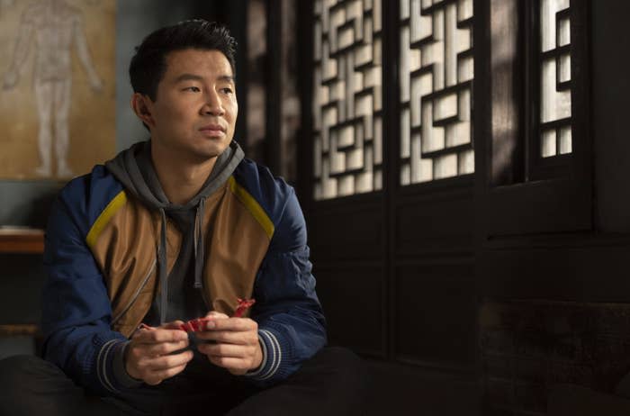 Shang-Chi, wearing a hoodie and a jacket, sitting in a scene from the film