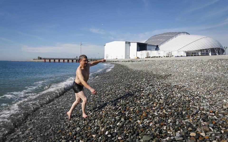 A man walks out of the sea after swimming during a sunny day as the Olympic Park is seen in the background, during the 2014 Winter Olympic Games in Sochi February 12, 2014. REUTERS/Shamil Zhumatov