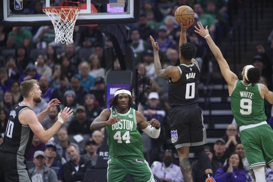 Sacramento Kings guard Malik Monk (0) shoots from between Boston Celtics center Robert Williams III (44) and guard Derrick White (9) during the first quarter of an NBA basketball game in Sacramento, Calif., Tuesday, March 21, 2023. (AP Photo/Randall Benton)