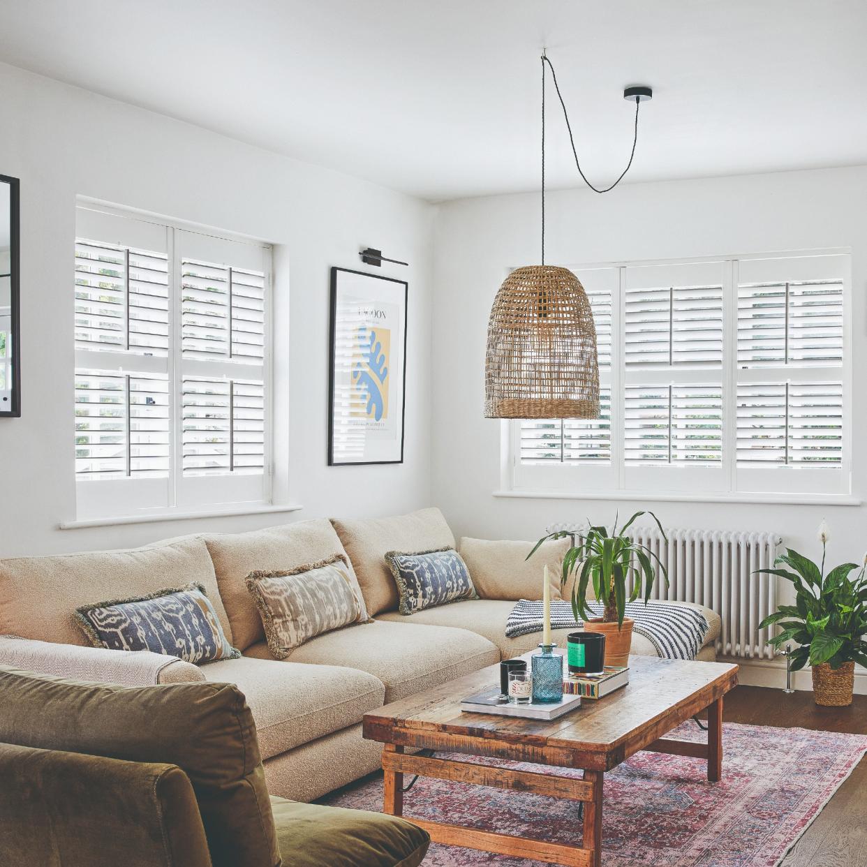  A living room with shutter-covered windows and a large beige sofa placed on a patterned Moroccan rug. 