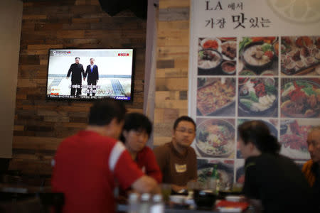 People sit beside a television screen with news of the inter-Korean summit between North Korea’s Kim Jong Un and South Korean President Moon Jae-in, in Koreatown, Los Angeles, California, April 27, 2018. REUTERS/Lucy Nicholson