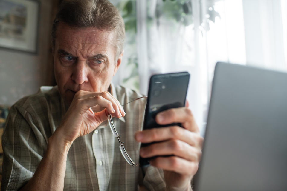 Senior man looking seriously at smartphone. If someone is asking for a payment over the phone or email — you should verify the caller's identity. (Getty)