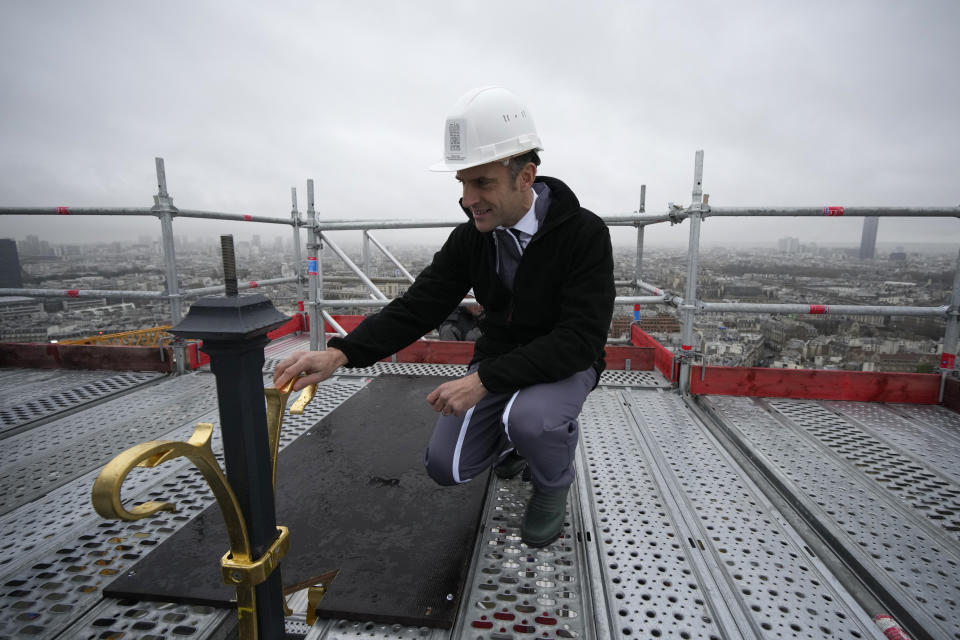 French President Emmanuel Macron touches the cross installed at the top of the spire of Notre Dame de Paris cathedral, Friday, Dec. 8, 2023 in Paris. French President Emmanuel Macron is visiting Notre Dame Cathedral on Friday, marking the one-year countdown to its reopening in 2024 following extensive restoration after the fire four years ago. (AP Photo/Christophe Ena, Pool)