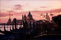 Gondolas are moored against a dramatic Venetian skyline.