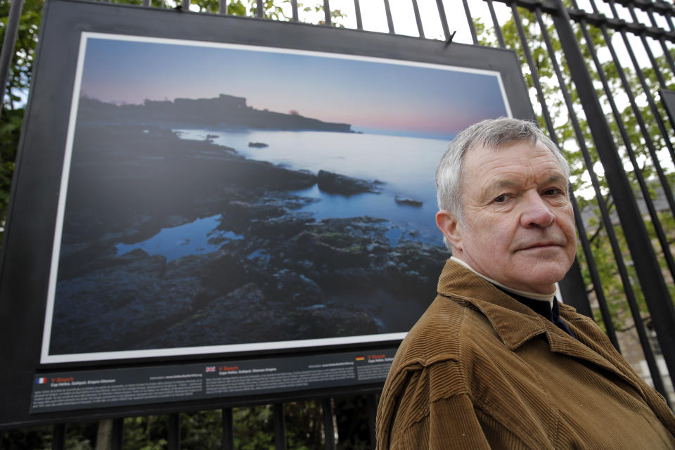 British photographer Michael St Maur Sheil poses in front of one of his pictures displayed at the Paris Luxembourg gardens, Tuesday, April 8, 2014, as part of an exhibition " Fields of Battle - Lands of Peace 14-18 ". The picture displayed is a modern take at the location of the Cape Helles landings on the Gallipoli peninsula. Captured over a period of seven years, Michael’s photography combines a passion for history and landscape and presents a unique reflection on the transformation of the battlefields of the Great War into the landscape of modern Europe. (AP Photo/Christophe Ena)