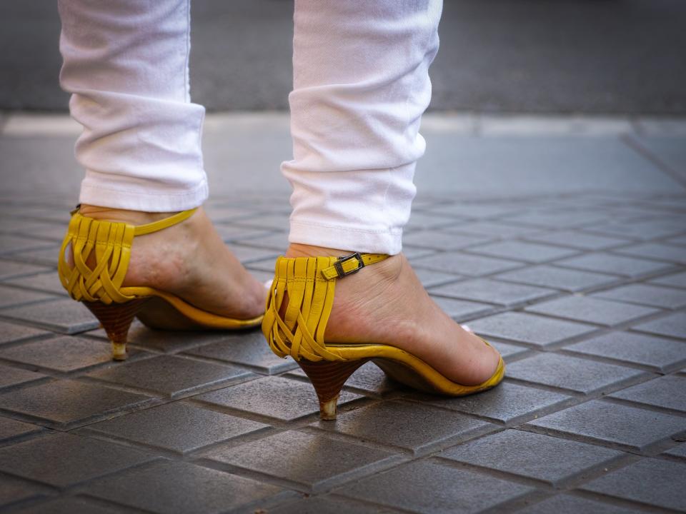 Woman wearing kitten-heeled yellow sandals with white pants.