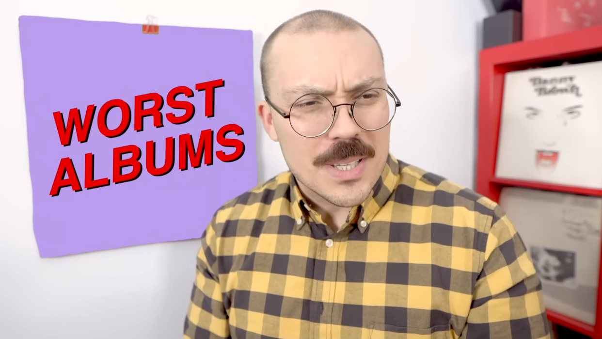  Anthony Fantano looks quizzical in front of a square reading 'worst albums'. 