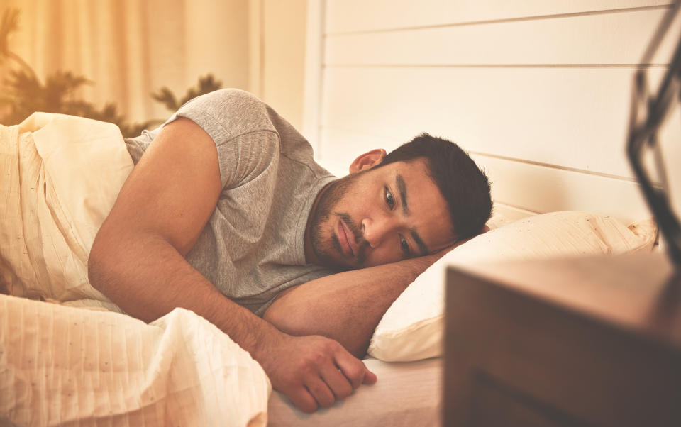 A man lies in bed, propped on one elbow, looking contemplative