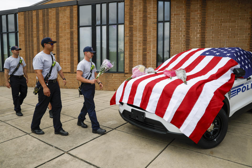 Charlotte firefighters from Engine 7 bring flowers to a flag-covered Charlotte-Mecklenburg police vehicle at the North Tryon Station in Charlotte, N.C., Tuesday, April 30, 2024, where Charlotte-Mecklenburg Officer Joshua Eyer was stationed. Police in North Carolina say a shootout that killed several law enforcement officers, including Eyer, and wounded others began as officers approached the home on Monday, to serve a warrant for a felon wanted for possessing a firearm. (AP Photo/Nell Redmond)