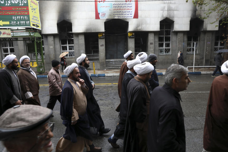 Clerics attend a funeral procession for Revolutionary Guard member Morteza Ebrahimi, walking past a bank building which burned in recent protests, in Shahriar, Iran, some 40 kilometers (25 miles) southwest of the capital, Tehran, Wednesday, Nov. 20, 2019. Ebrahimi was killed during protests over government-set fuel prices rising last week, demonstrations that quickly spiraled in violence. (AP Photo/Vahid Salemi)