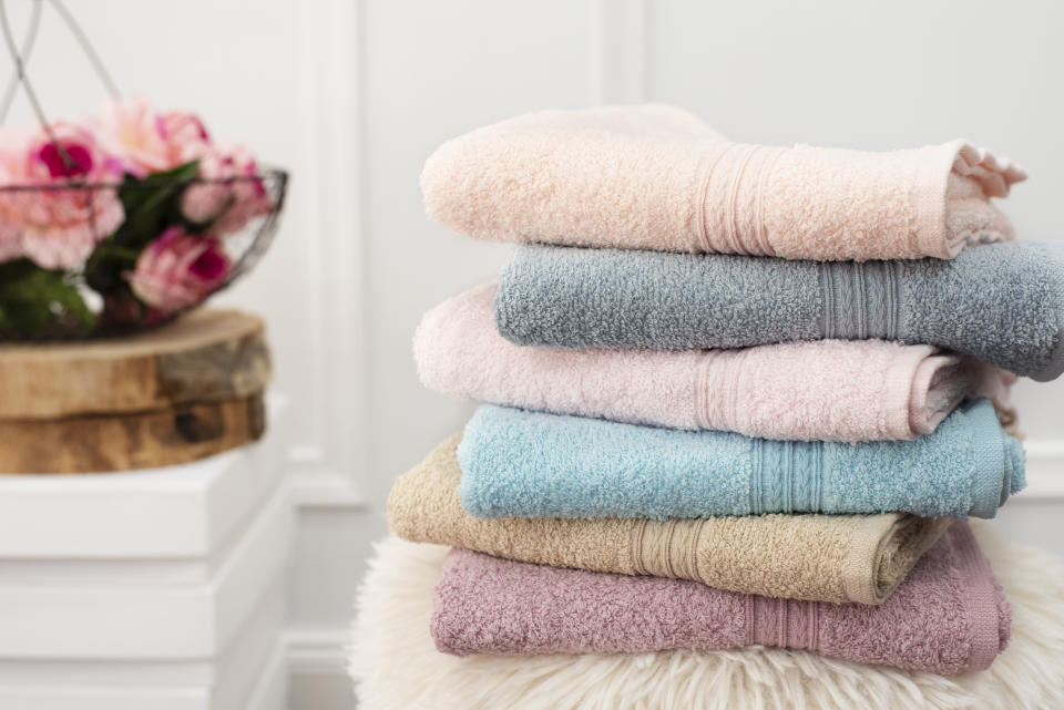 A stack of colourful towels in a bathroom with a basket of flowers in the background