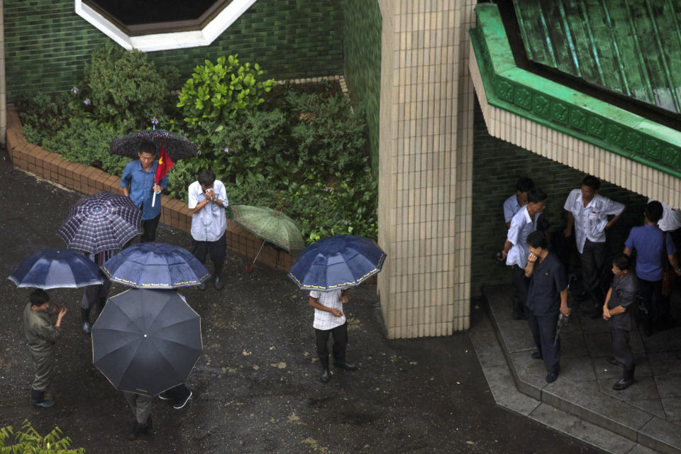 Residents gather under umbrellas and shelter as rain falls in Pyongyang, North Korea, Friday, Aug. 24, 2018. Rain from Typhoon Soulik fell in North Korea's capital Pyongyang throughout the morning, but the impact appeared to be mild. Information on what preparations had been taken or if any damage had occurred in the North was not immediately available.(AP Photo/Ng Han Guan)