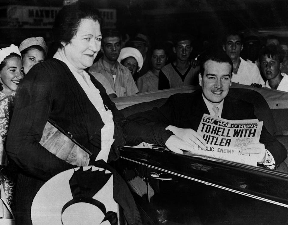 Black-and-white photo of seated man smiling and holding the Hobo News with the headline "To Hell With Hitler: Public Enemy No 1"