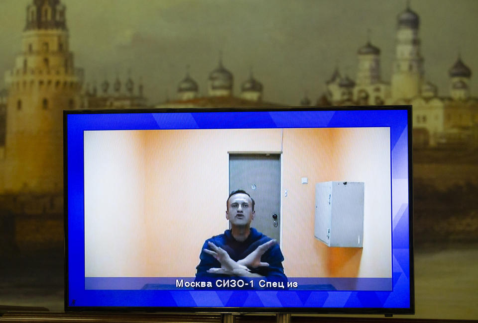 Russian opposition leader Alexei Navalny appears on a TV screen during a live session with the court during a hearing of his appeal in a court in Moscow, Russia, Thursday, Jan. 28, 2021, with an image of the Moscow Kremlin in the background. Navalny was jailed soon after arriving to Moscow after authorities accused him of violating of the terms of his 2014 fraud conviction. A court on Thursday is to hear an appeal on the ruling to remand him into custody. Next week, another court will decide whether to send him to prison for several years for the alleged violations. (AP Photo/Alexander Zemlianichenko)