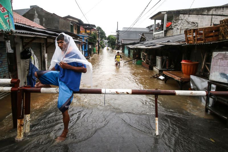 A man wearing a plastic sheet travels along a flooded street at Pondok Maharta residence, South Tangerang, near Jakarta