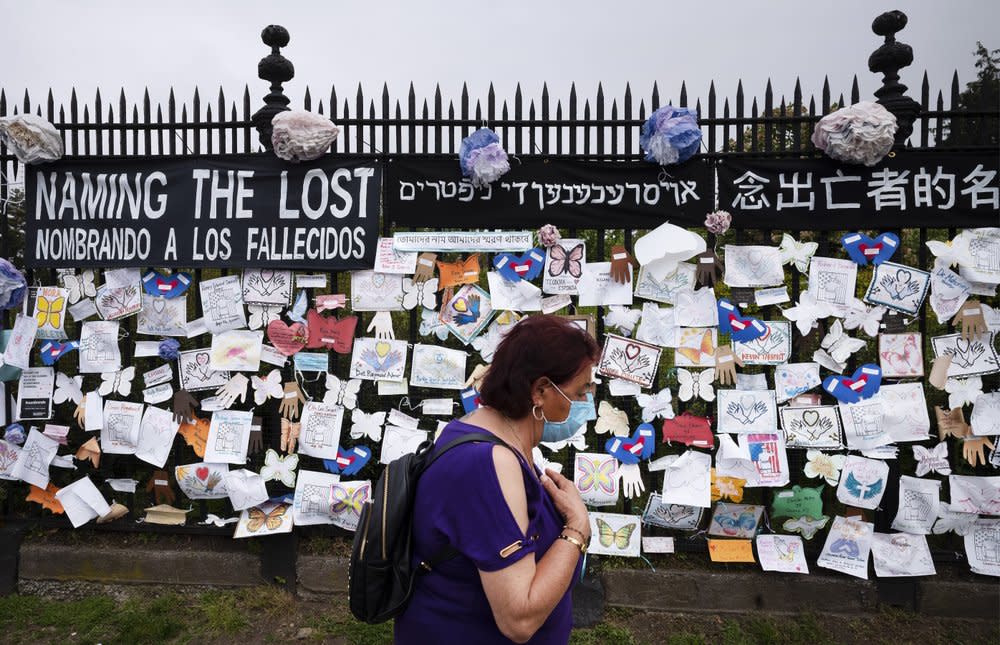 In this May 28, 2020, file photo, a woman passes a fence outside Brooklyn’s Green-Wood Cemetery adorned with tributes to victims of COVID-19 in New York. (AP Photo/Mark Lennihan, File)
