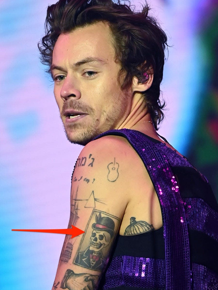 A red arrow pointing to a skeleton tattoo on Harry Styles' left arm.