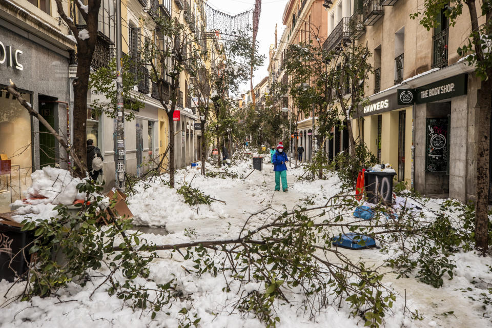 People walk along a street with snow and fallen tree branches during after a heavy snowfall in downtown Madrid, Spain, Sunday, Jan. 10, 2021. A large part of central Spain including the capital of Madrid are slowly clearing snow after the country's worst snowstorm in recent memory. (AP Photo/Manu Fernandez)