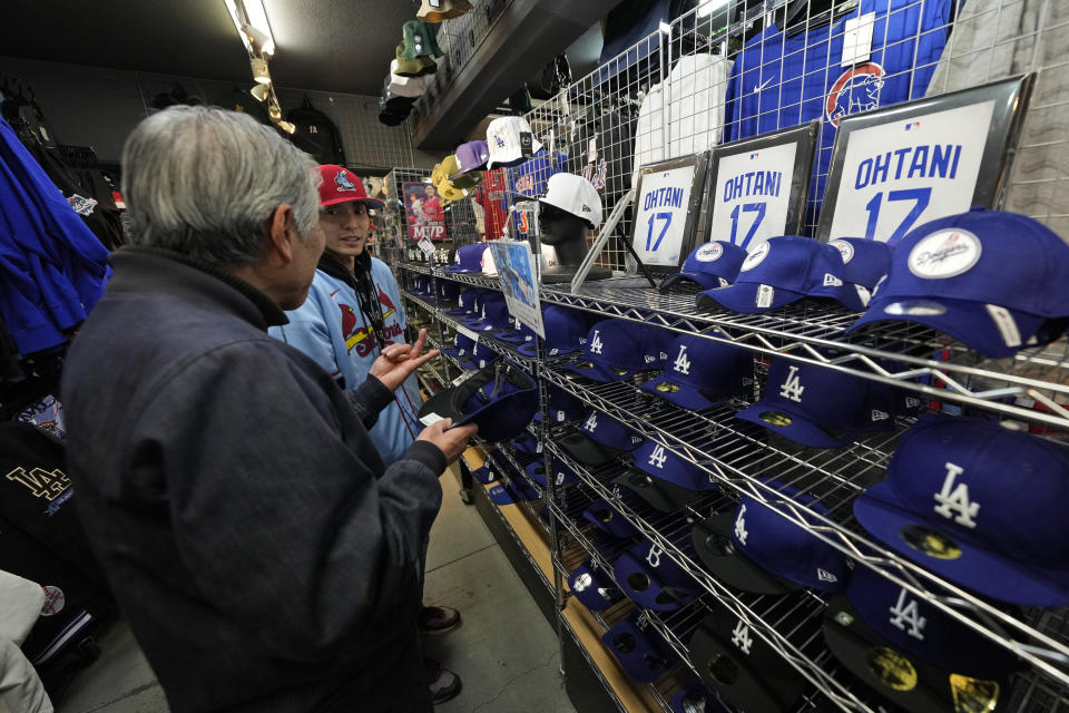 A store clerk helps a customer choose baseball hats with different designs showing the name of Shohei Ohtani of the Los Angeles Dodgers at SELECTION, a sporting goods store in Shinjuku district of Tokyo, Thursday, Feb. 29, 2024. (AP Photo/Hiro Komae)