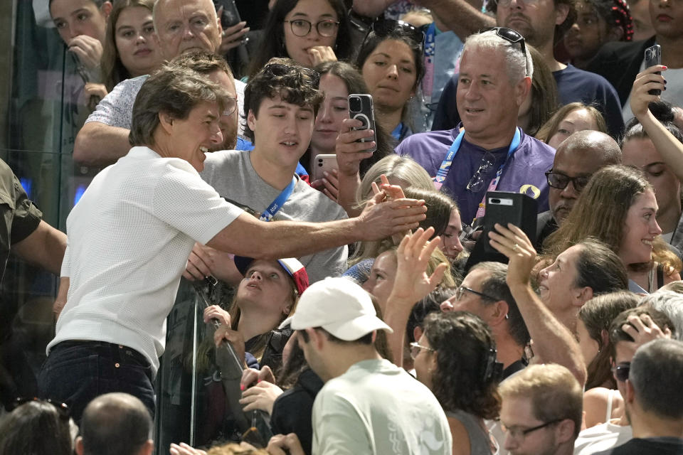 El actor Tom Cruise, izquierda, interactúa con los fans mientras asiste a la ronda de clasificación de gimnasia artística femenina en los Juegos Olímpicos de Verano de 2024, el domingo 28 de julio de 2024, en París, Francia. (Foto AP/Charlie Riedel)