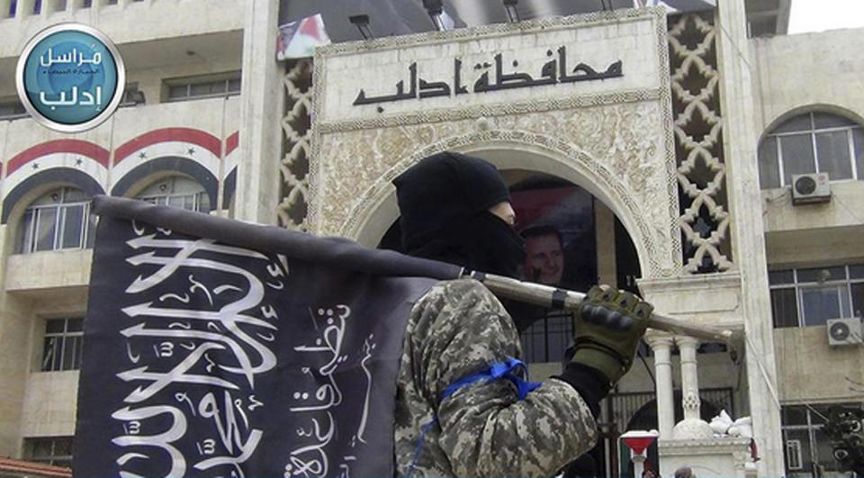 FILE - In this file photo posted on the Twitter page of Syria's al-Qaida-linked Nusra Front on March 28, 2015, a fighter from Syria's al-Qaida-linked Nusra Front holds his group flag as he stands in front of the governor building in Idlib province, north Syria. As the decisive battle for Idlib looms, a motley crew of tens of thousands of Syrian opposition fighters, including some of the world's most radical, are digging their heels_ looking for ways to salvage what is possible of an armed rebellion that at one point in the seven-year conflict controlled more than half of the country. (Al-Nusra Front Twitter page via AP, File)