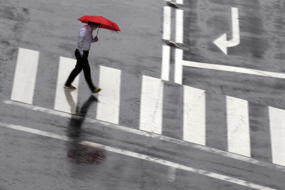 A man wearing a protective mask to help curb the spread of the coronavirus walks along a pedestrian crossing in a sudden rain Thursday, June 17, 2021, in Tokyo. (AP Photo/Eugene Hoshiko)