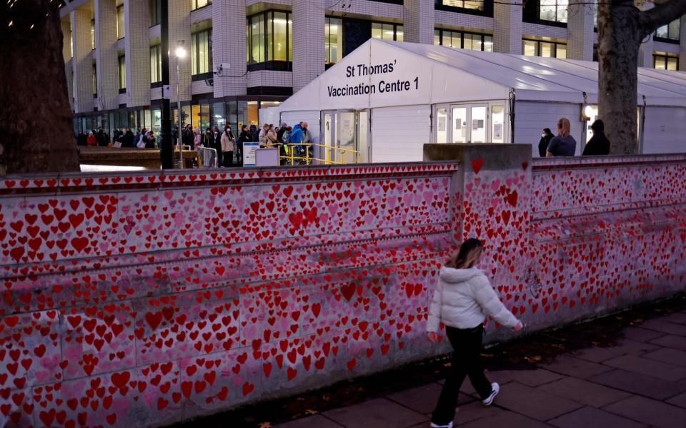  Members of the public are pictured beyond hearts painted on the National Covid Memorial Wall, as they queue to receive a dose of a Covid-19 vaccine - Tolga Akmen/AFP