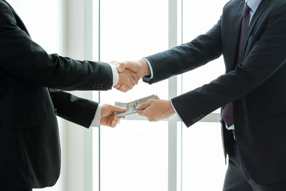 Businessman taking money while shaking hands.