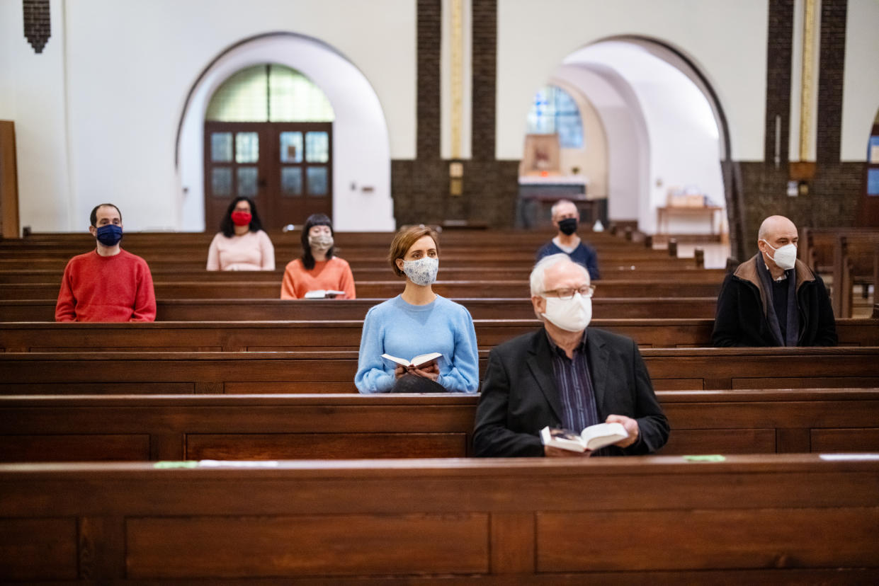 People wearing protective face masks sitting with social distance and  attending religious mass at church. Group of people at church congregation.