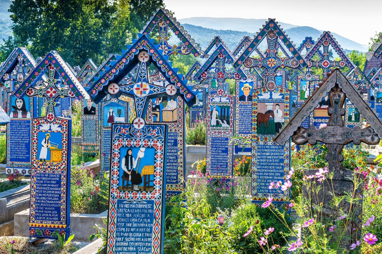 Merry Cemetery, Săpânţa, Romania, elaborate painted blue tombstones with poetry and images in little gardens for each grave with mountains in the distance on a bright sunny summer day