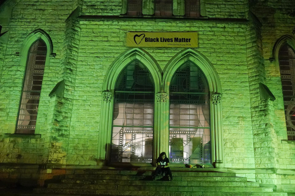 A lone protester sits on the steps of a church, Friday, Sept. 25, 2020, in Louisville. Breonna Taylor's family demanded Friday that Kentucky authorities release all body camera footage, police files and the transcripts of the grand jury hearings that led to no charges against police officers who killed the Black woman during a March drug raid at her apartment. (AP Photo/Darron Cummings)