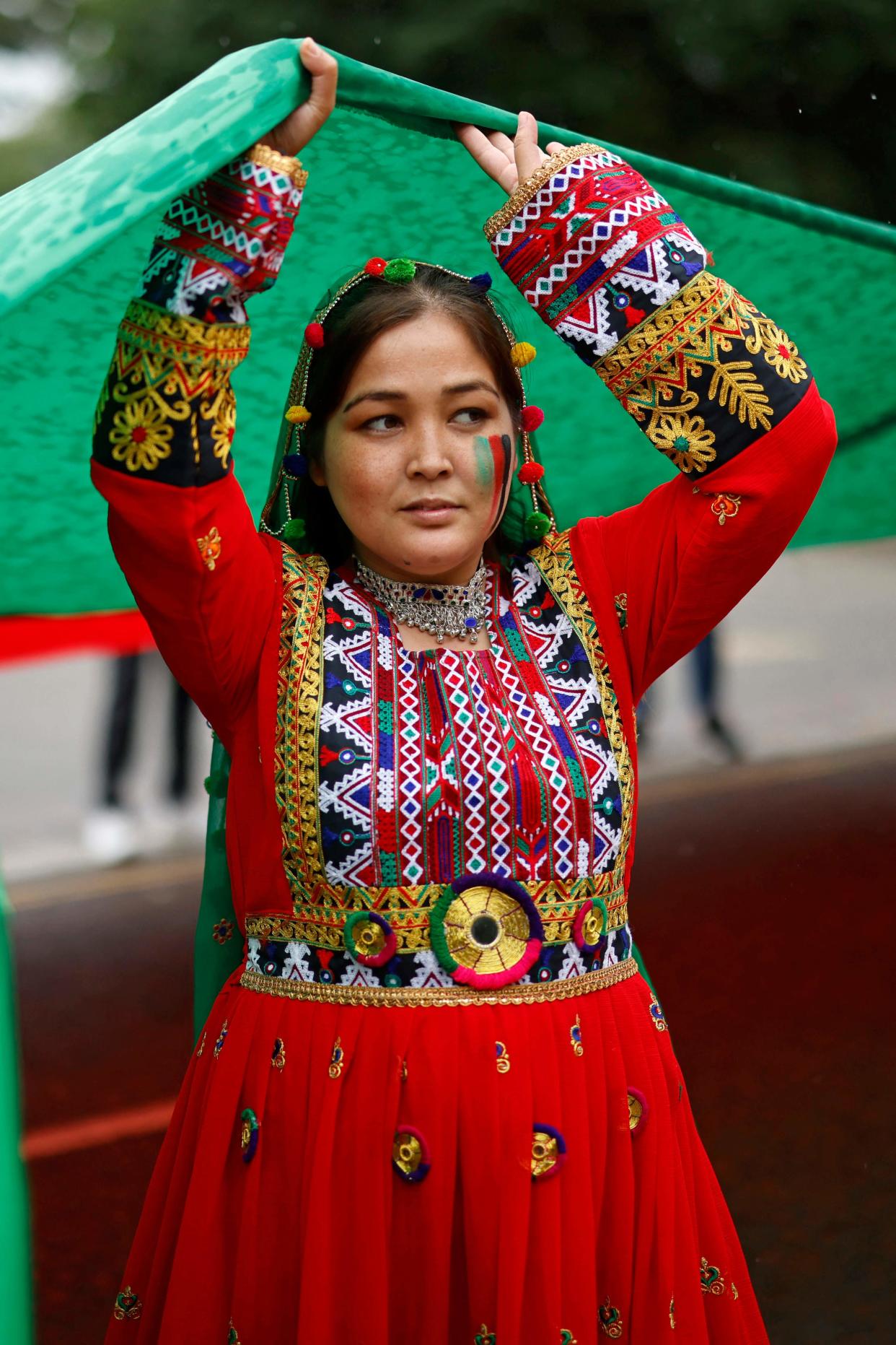 A woman wearing traditional Afghan costume holds up a large flag people as gather at Marble Arch ahead of a march in solidarity with the people of Afganistan, in central London on August 21, 2021. (Photo by Tolga Akmen / AFP) (Photo by TOLGA AKMEN/AFP via Getty Images) ORG XMIT: 0 ORIG FILE ID: AFP_9LF7TP.jpg