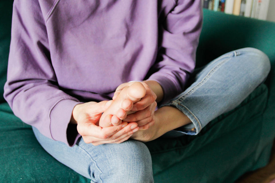 Person sitting cross-legged on a sofa, hands together resting on knees