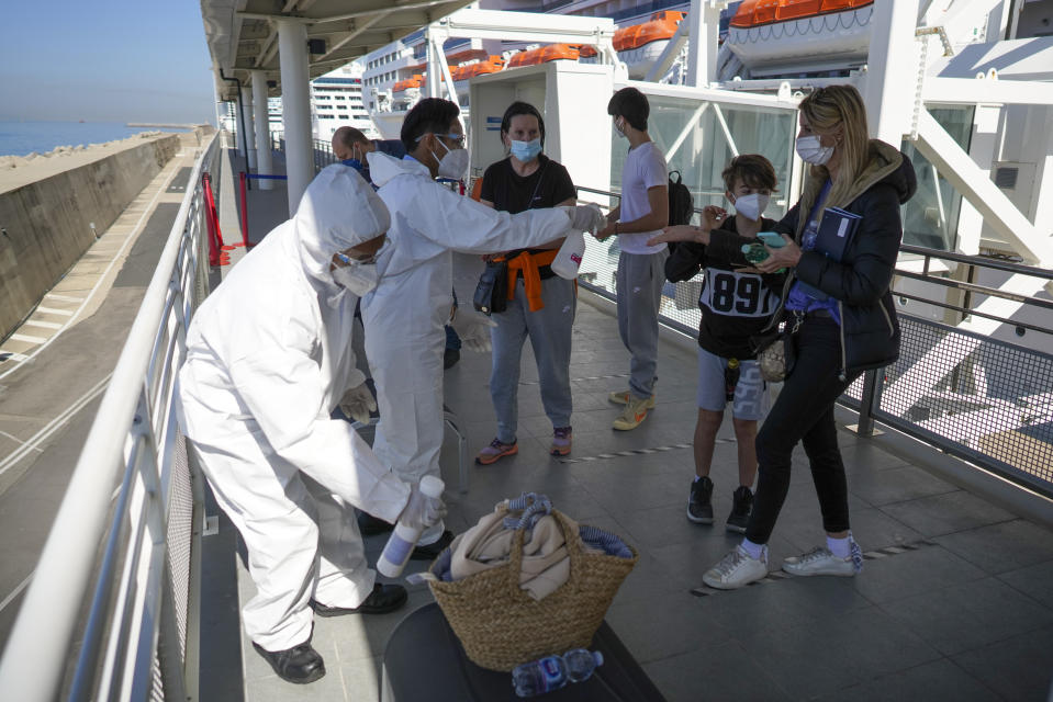 Passengers, from right, Stefania Battistoni, her sons Dasteen and Samuel Pacifici and her mother Loredana Merlo have their hand luggage sanitized prior to boarding the MSC Grandiosa cruise ship in Civitavecchia, near Rome, Wednesday, March 31, 2021. MSC Grandiosa, the world's only cruise ship to be operating at the moment, left from Genoa on March 30 and stopped in Civitavecchia near Rome to pick up more passengers and then sail toward Naples, Cagliari, and Malta to be back in Genoa on April 6. For most of the winter, the MSC Grandiosa has been a lonely flag-bearer of the global cruise industry stalled by the pandemic, plying the Mediterranean Sea with seven-night cruises along Italy’s western coast, its major islands and a stop in Malta. (AP Photo/Andrew Medichini)