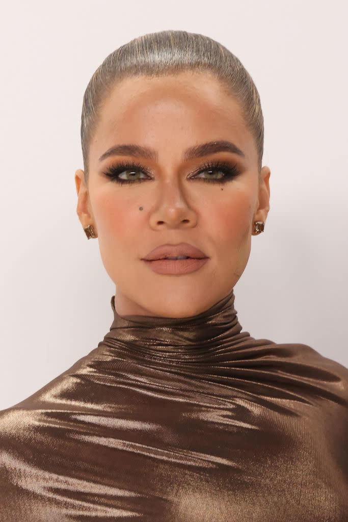 Close-up of Khloe Kardashian wearing a shiny metallic high neck top, with sleeked-back hair and dramatic eye makeup