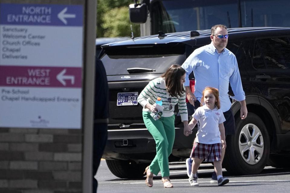 A girl in a school uniform walks with two adults.