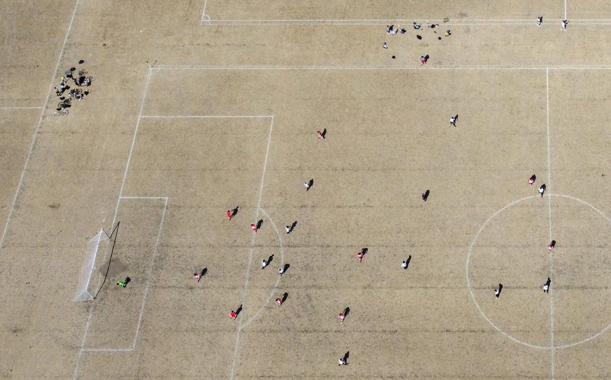 An amateur football game goes ahead on a parched grass pitch at London's Hackney Marshes during Sunday's heatwave - TOBY MELVILLE 