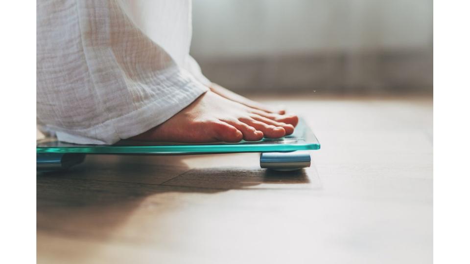 Female feet standing on electronic scales for weight control on wooden background. The concept of slimming and weight loss