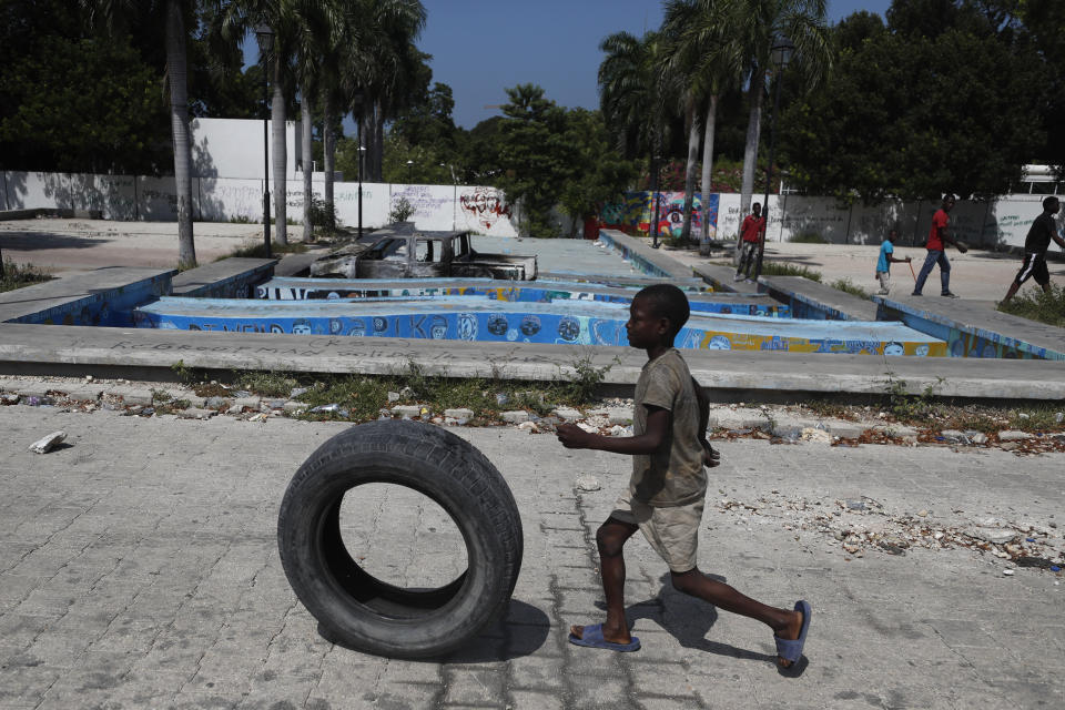 A boy rolls a tire through the Champ de Mars park as protesters prepare to set tires alight in front of the entrance to the National Palace, in Port-au-Prince, Haiti, Monday, Oct. 14, 2019. Haiti's embattled president faced a fifth week of protests on Monday as road blocks went up across the country after opposition leaders said they will not back down on their call for Jovenel Moïse to resign.(AP Photo/Rebecca Blackwell)