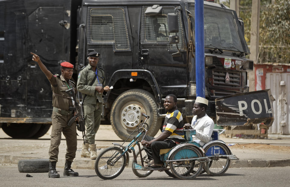 Security forces direct two disabled men in hand-pushed wheelchairs away from a road which has been closed to vehicles for security reasons, leading to the electoral commission offices in Kano, northern Nigeria Monday, Feb. 25, 2019. Nigeria is counting votes in its presidential election and observers are giving mixed assessments of the process. (AP Photo/Ben Curtis)