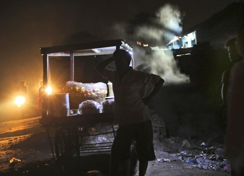 In this Oct. 22, 2019, photo, a vendor stands next to his food cart as smoke rises from a recently collapsed house due to land subsidence in the village of Liloripathra in Jharia, a remote corner of eastern Jharkhand state, India. The fires started in coal pits in eastern India in 1916. More than a century later, they are still spewing flames and clouds of poisonous fumes into the air, forcing residents to brave sizzling temperatures, deadly sinkholes and toxic gases. (AP Photo/Aijaz Rahi)