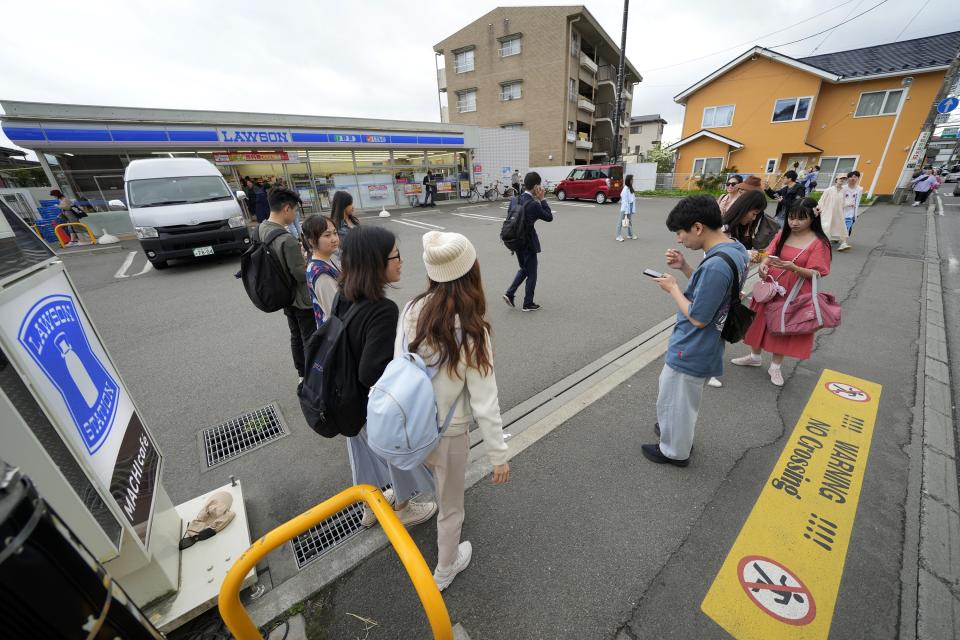 Tourists gather in front of the Lawson convenience store, a popular photo spot framing a picturesque view of Mt. Fuji in the background on cloudy evening of Tuesday, April 30, 2024, at Fujikawaguchiko town, Yamanashi Prefecture, central Japan. The town of Fujikawaguchiko, known for a number of popular photo spots for Japan's trademark of Mt. Fuji, on Tuesday began to set up a huge black screen on a stretch of sidewalk to block view of the mountain in a neighborhood hit by a latest case of overtourism in Japan. (AP Photo/Eugene Hoshiko)